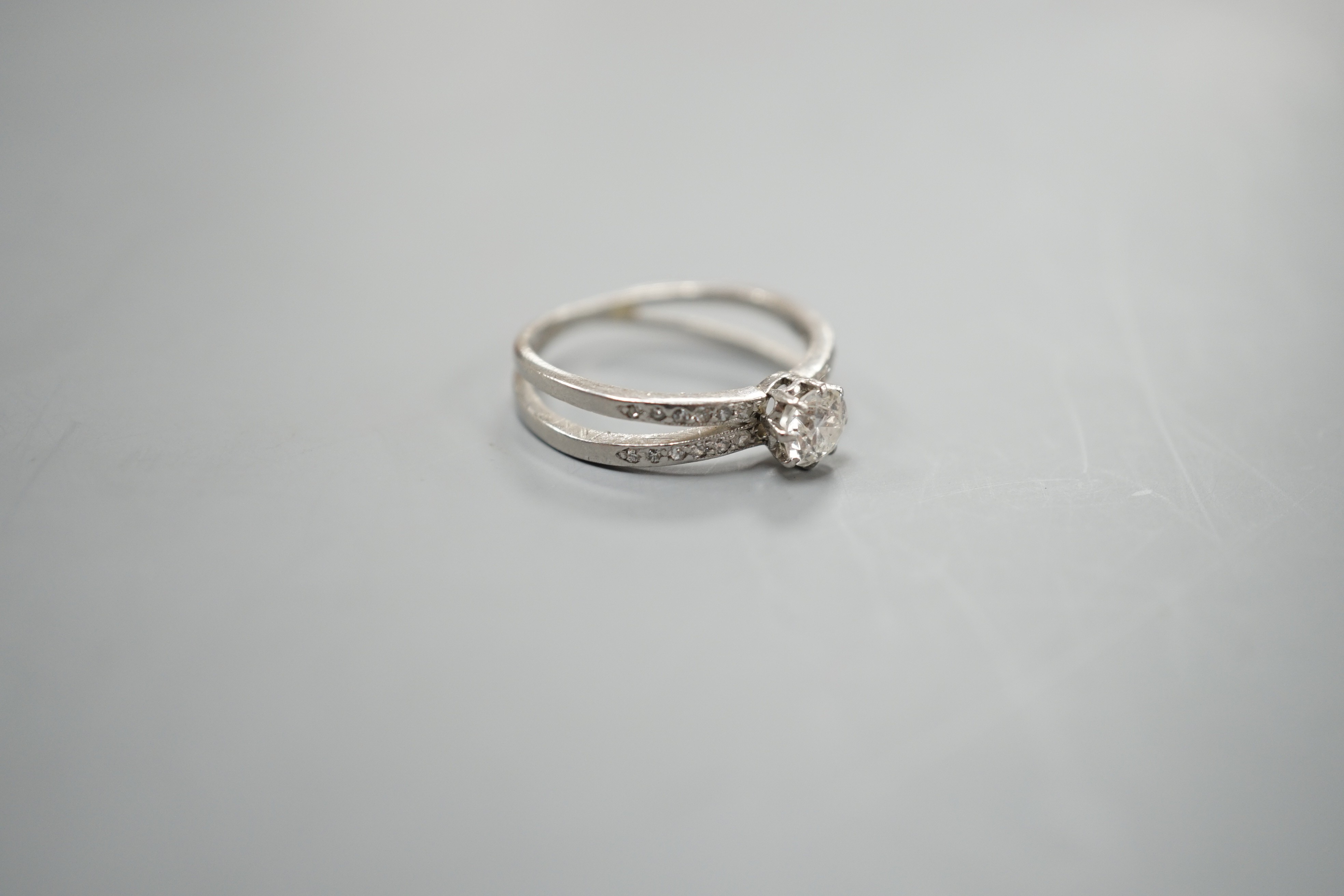 A modern white metal and single stone diamond ring, with diamond chip set crossover shoulders, size K, gross weight 3.3 grams.